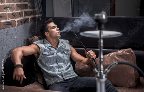 Sexy guy relaxes in a hookah in the shisha bar.