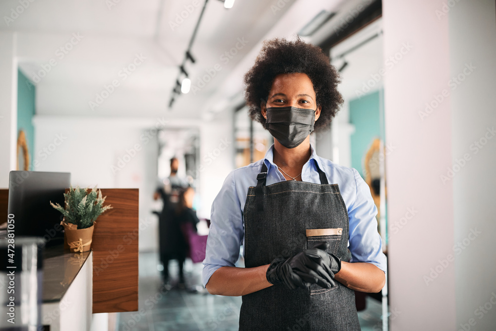 African American hair salon owner wears protective face mask at her reopened salon and looking at camera. African American hair salon owner wears protective face mask at her reopened salon and looking at camera.