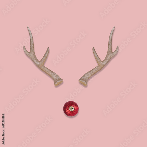 Fotografia Abstract Christmas reindeer face made with antlers and a bauble decoration nose on a pastel pink background
