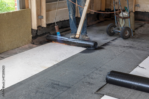 Installation of waterproofing on the concrete foundation by heating and melting rolls of bitumen roofing felt with a propane blowtorch photo