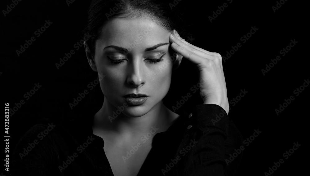 Business strong thinking woman find the answer in clever mind with closed eyes with fingers near the face in black t-shirt on dark shadow black background. Closeup front view Business strong thinking woman find the answer in clever mind with closed eyes with fingers near the face in black t-shirt on dark shadow black background. Closeup front view