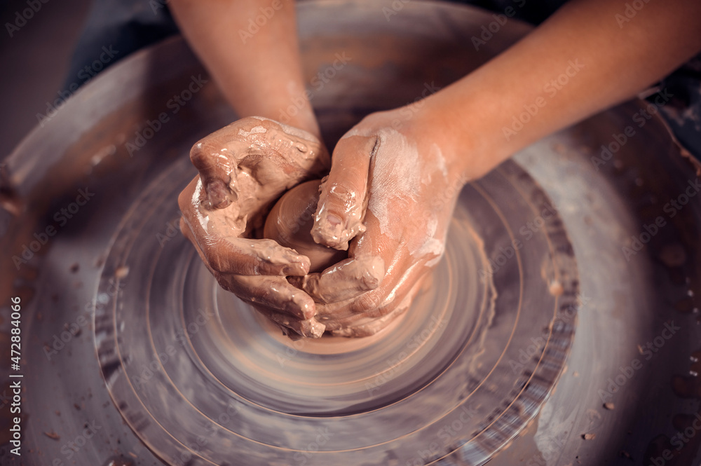 The potter's hands are shaped a cup from a clay. The process of creating pottery on a potter's wheel. The master ceramist works in his studio. Close-up, only hands. Crockery from clay own hands.