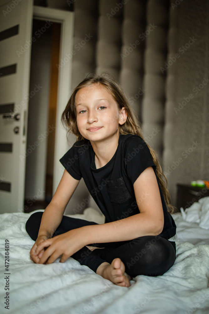 Front view portrait of a happy teen girl sitting on bed in the bedroom