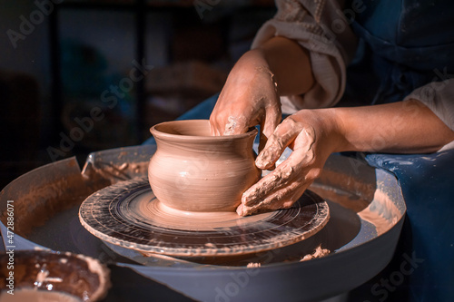 Close-up A woman potter in beautifully sculpts a deep bowl of brown clay and cuts off excess clay on a potter's wheel in a beautiful workshop