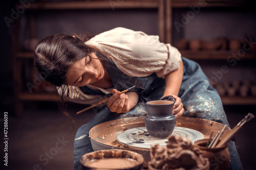 Beautiful young woman master demonstrates the process of making ceramic dishes using the old technology. Folk handicraft.
