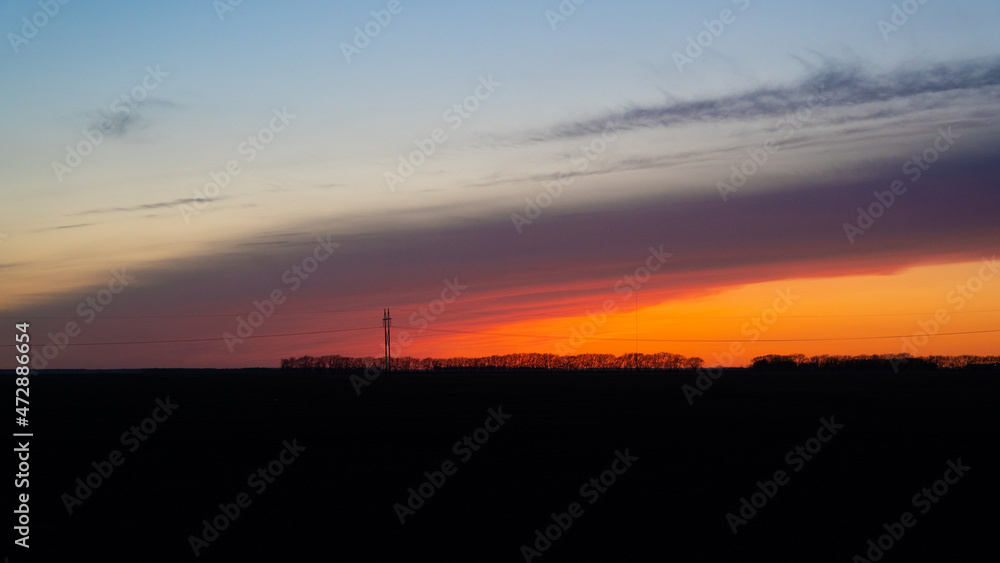 Beautiful orange and pink sunset in rural North Dakota with dark foreground. Trees are silhouettes. Colors blending.