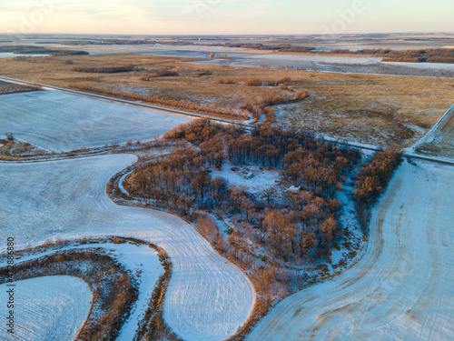 Aerial view of winter trees, frozen, snowy farmland and cultivated fields in rural North Dakota. Winter, sunset. Vast expanse with no one.