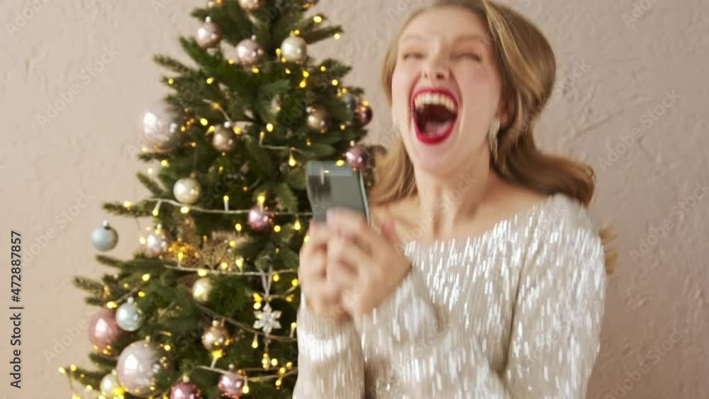 Amazed lucky christmas woman using mobile phone looks and sees the message with a good news. Happy female is surprised, rejoices and celebrate win. Amazed lucky christmas woman using mobile phone looks and sees the message with a good news. Happy female is surprised, rejoices and celebrate win.