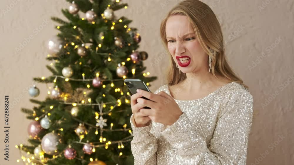 Angry festive blonde woman in a shiny evening dress typing on smart phone negative message emotionally. Bad feedback rating service, obsession relationship. Agressive person using mobile Angry festive blonde woman in a shiny evening dress typing on smart phone negative message emotionally. Bad feedback rating service, obsession relationship. Agressive person using mobile