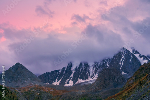 Purple sunset over majestic mountains. Sunset in magenta tones. Atmospheric purple landscape with a high-altitude snowy mountain valley.