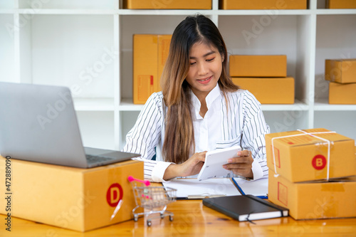 Asian Women business owner working at home with packing box on the workplace - online shopping SME entrepreneur or freelance working concept