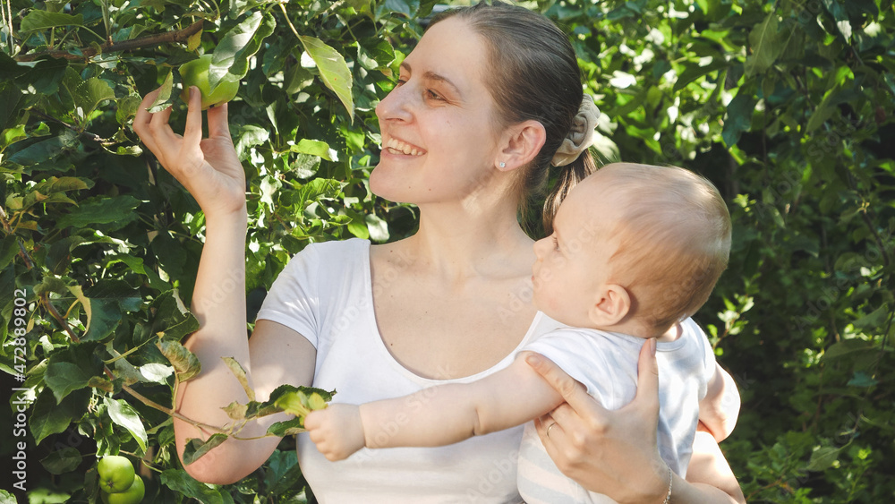 Portrait of little baby boy with young mother picking green ripe apples at domestic garden Portrait of little baby boy with young mother picking green ripe apples at domestic garden
