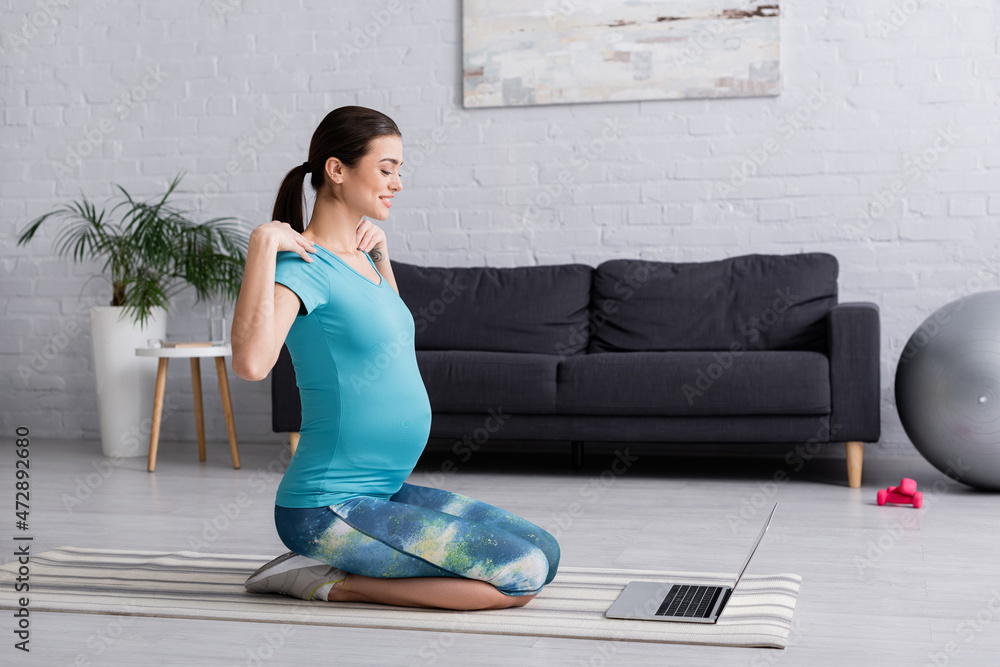 smiling pregnant woman in sportswear working out while looking at laptop.