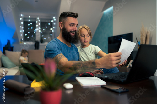 Young businessman working at home while using laptop and his daughter interrupts him