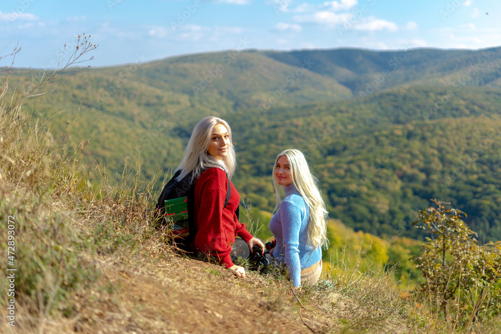 Two beautiful blonde woman walking in the mountain during a sunny day