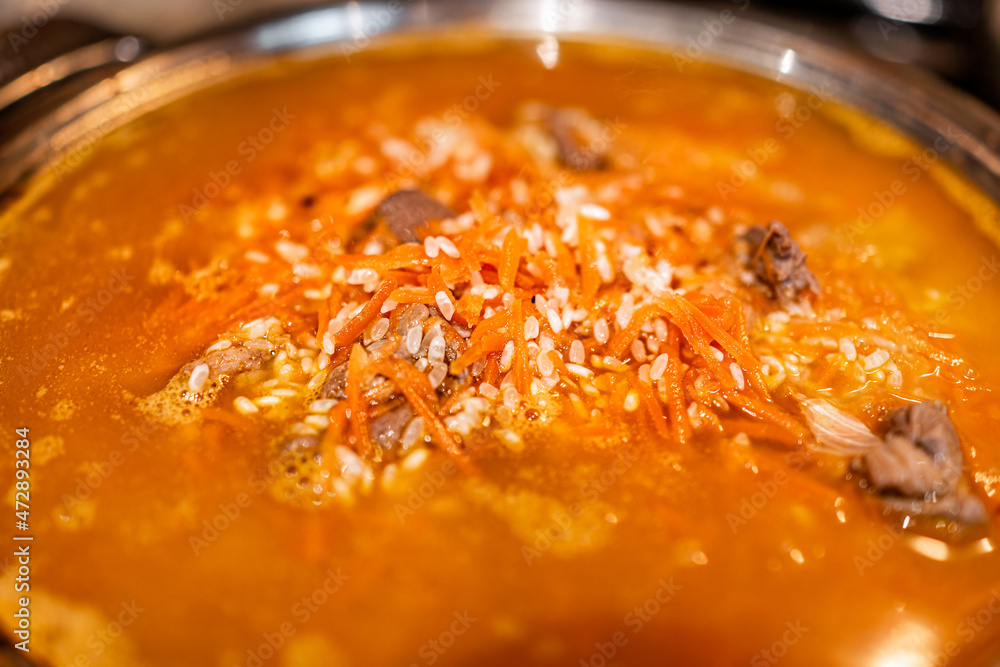 Lamb meat cooking with carrots on frying pan with rice as traditional Kazakh or Uzbek pilaf or plov macro closeup with orange color Lamb meat cooking with carrots on frying pan with rice as traditional Kazakh or Uzbek pilaf or plov macro closeup with orange color