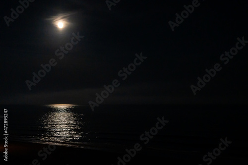 Big full moon rising above sea Atlantic ocean at dark night with lunar light path reflected on water with clouds in Myrtle Beach, South Carolina