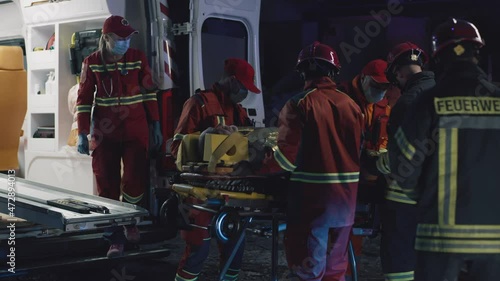 Multiracial emergency service workers carrying survivor and putting carrier into ambulance car during rescue mission on disaster site at night