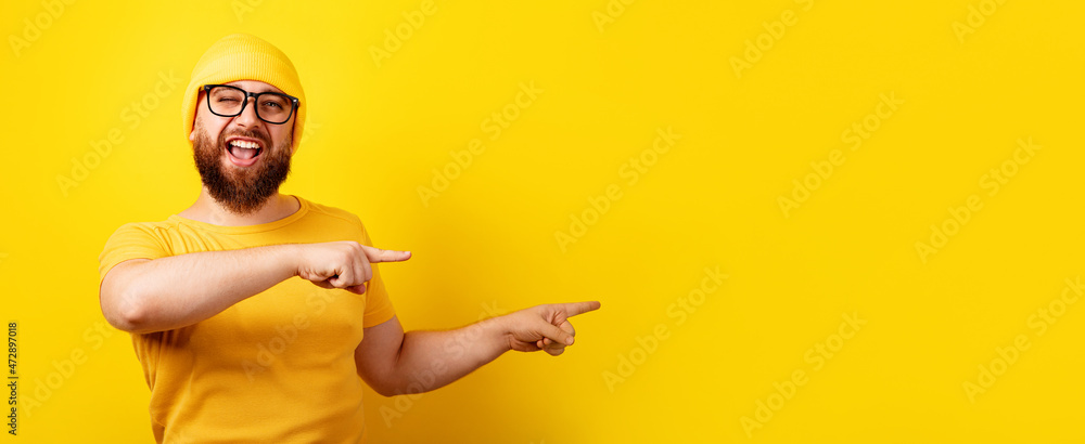 smiling bearded man in glasses point index fingers over yellow background, panoramic layout with space for text smiling bearded man in glasses point index fingers over yellow background, panoramic layout with space for text