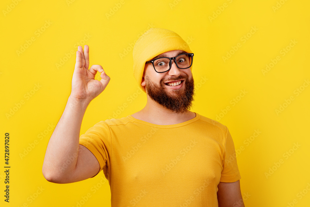 smiling bearded man in glasses showing ok gesture over yellow background
