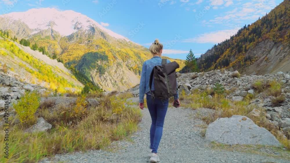young tourist walks through mountainous area and looks at beautiful landscape. She is dressed in denim suit, with bunch of hair on her head, enjoying views of autumn mountains. happy single. Hiking. young tourist walks through mountainous area and looks at beautiful landscape. She is dressed in denim suit, with bunch of hair on her head, enjoying views of autumn mountains. happy single. Hiking.