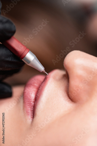 Young woman having permanent makeup on lips in beautician salon. Close up