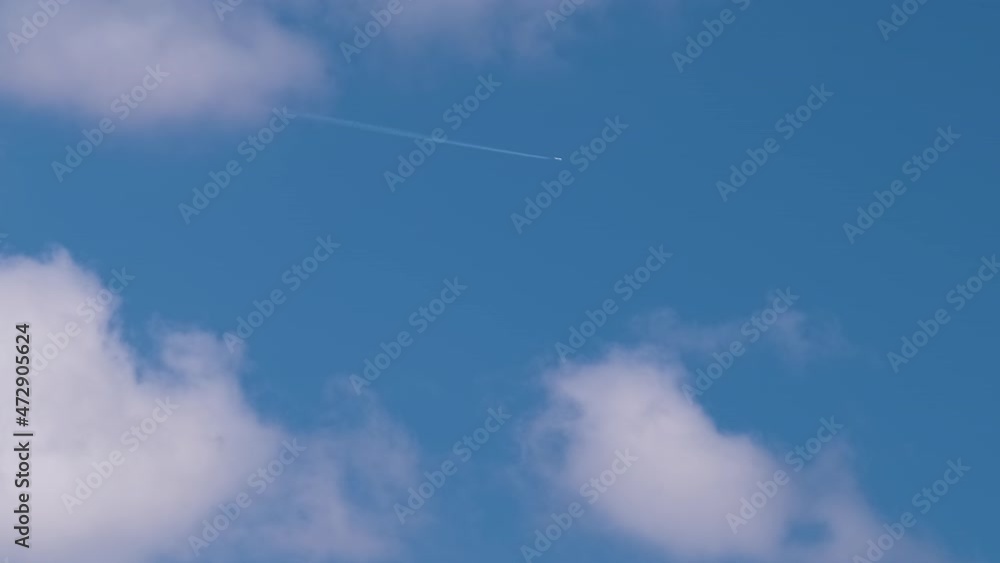 Distant passenger jet plane flying on high altitude on blue sky with white clouds leaving smoke trace of contrail behind. Air traveling concept Distant passenger jet plane flying on high altitude on blue sky with white clouds leaving smoke trace of contrail behind. Air traveling concept