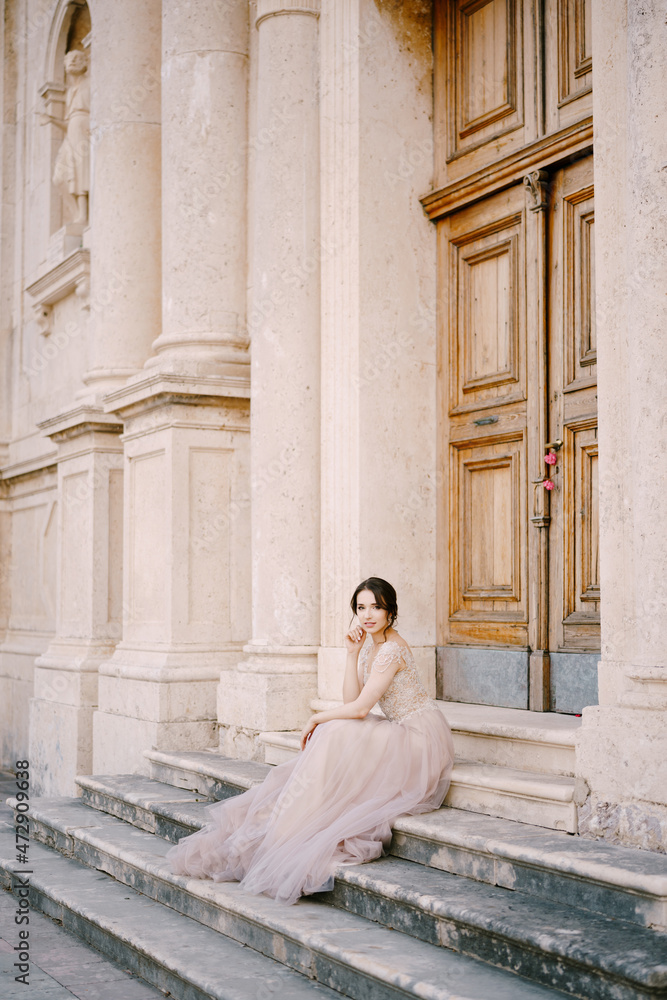 Bride sits on the steps of an old building in front of the entrance