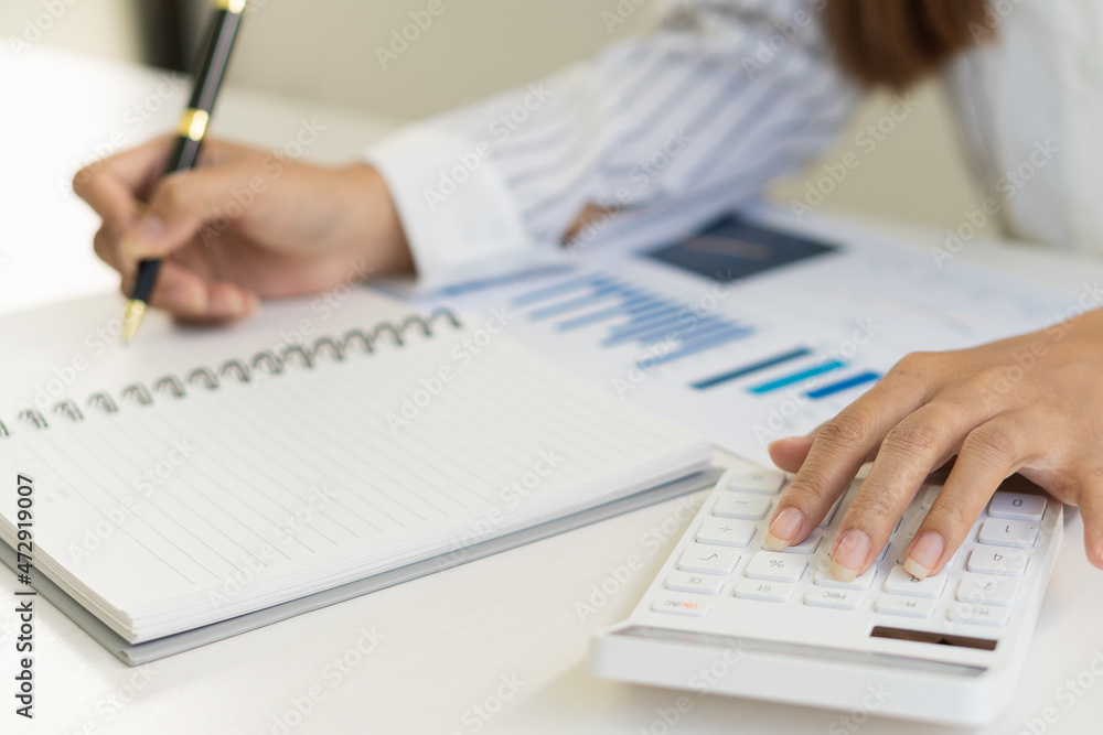 An accountant presses a calculating calculator to make a monthly financial report or company profit at his desk with graph papers and a work-from-home ideal laptop. An accountant presses a calculating calculator to make a monthly financial report or company profit at his desk with graph papers and a work-from-home ideal laptop.
