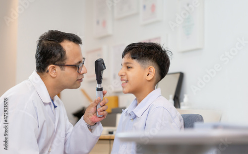 Smiling Indian boy doing eye test checking examination with optometrist in optical store
