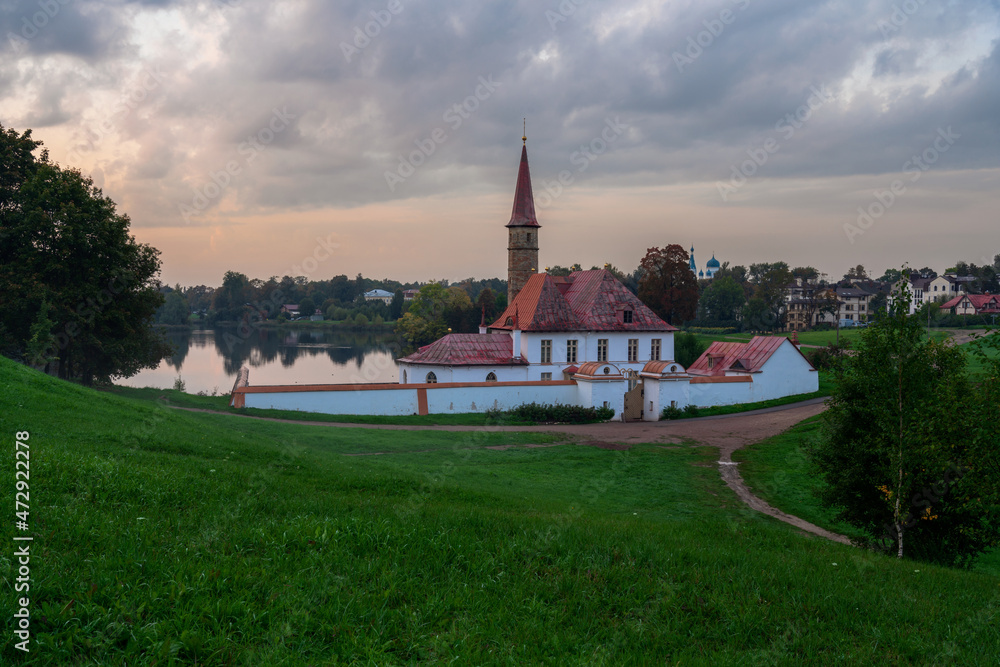 View of the Priory Palace on the shore of the Black Lake against the background of the sunset sky on an autumn foggy evening, Gatchina, St. Petersburg, Russia
