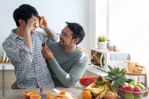 Lgbtq couples having fun together, covering his eyes with orange slices in the kitchen, spending time together