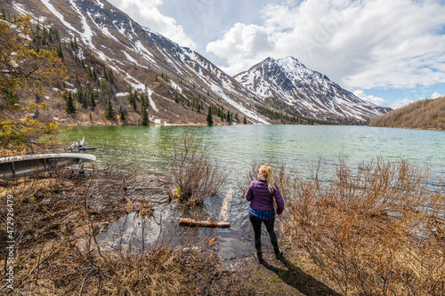 Hiker standing beside a pristine lake in northern Canada with a stunning snow capped mountain background landscape. Tourism, travel shot in Yukon Territory.  © Scalia Media
