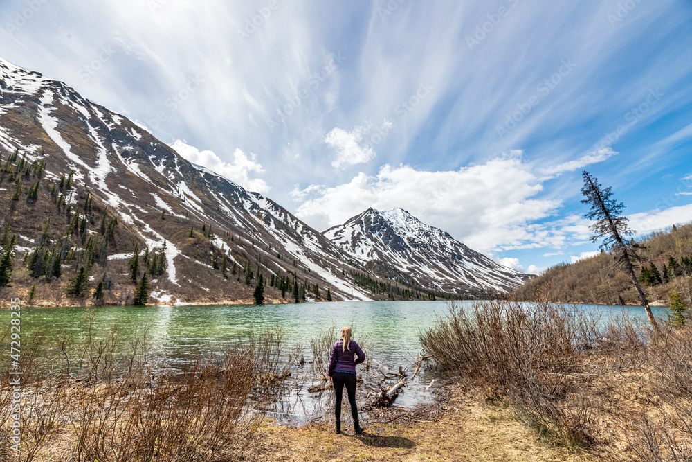 Tourism, travel shot of woman hiker standing beside a northern, isolated lake during spring time with stunning mountains, pristine lake in the background. 