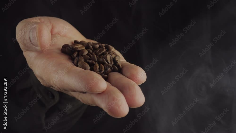 Fragrant freshly roasted coffee beans on a man's palm on a dark background with smoke. Fragrant freshly roasted coffee beans on a man's palm on a dark background with smoke.