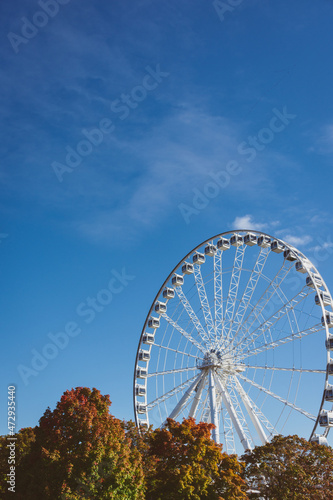 White ferris wheel and trees in red and orange autumn colours in old Montreal on a sunny day, blue sky and light clouds photo