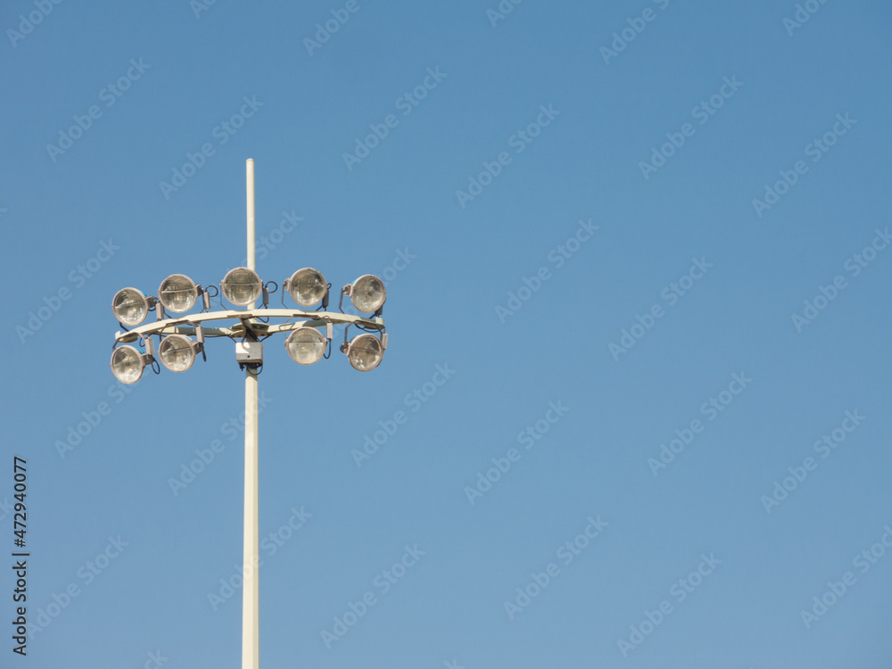 Stadium spotlight with ten lights standing against blue sky day.