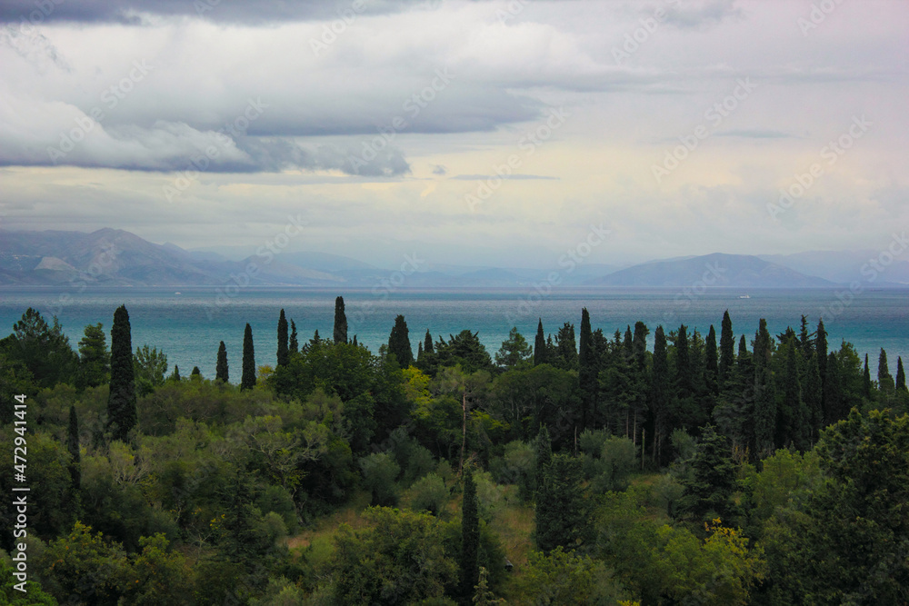 Panoramic Mediterranean landscape with green cypress and olive trees and turbulent stormy grey sky.