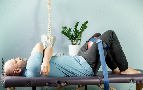 A man lying on the massage table in constructive rest postion with foam roller and malligan belt photo