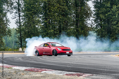 Red Drift Car / Race car drifting around corner very fast with lots of smoke from burning tires on speedway / racetrack / drift track. Infiniti g35 v8. JDM car. Luxury red sport car.