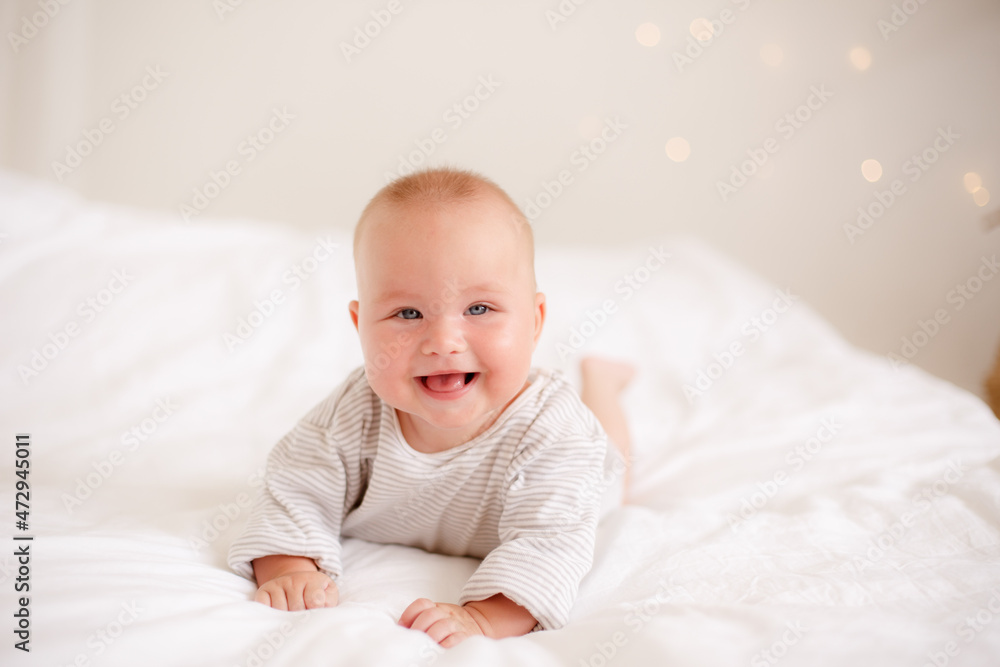 the baby is lying at home on the bed smiling