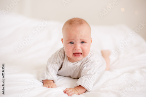 the baby is lying at home on the bed smiling