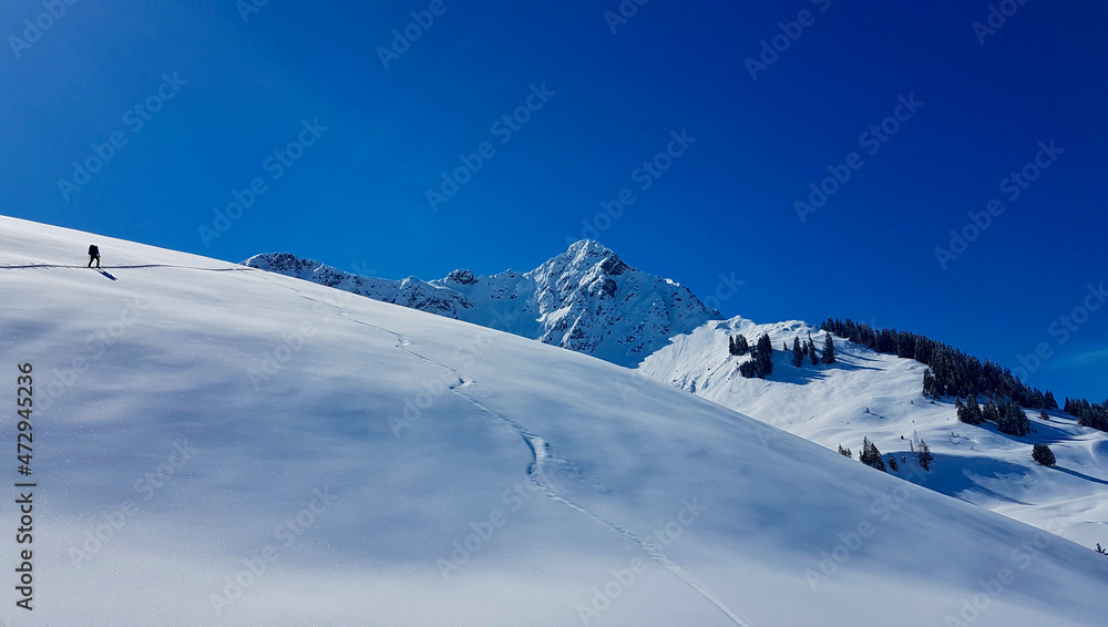 Ski mountaineer hiking up a summit in the Austrian Alps on a beautiful winter day. Walsertal, Vorarlberg, Austria.