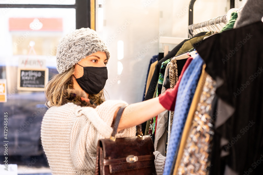 A customer with a protective mask looking at new collection clothes on a hanger, second-hand and sustainable clothing store, coronavirus, covid-19