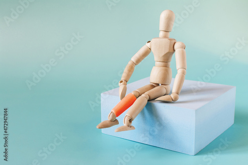 The figure of a wooden man on a blue podium with a leg highlighted in red on a light background. The concept of leg diseases