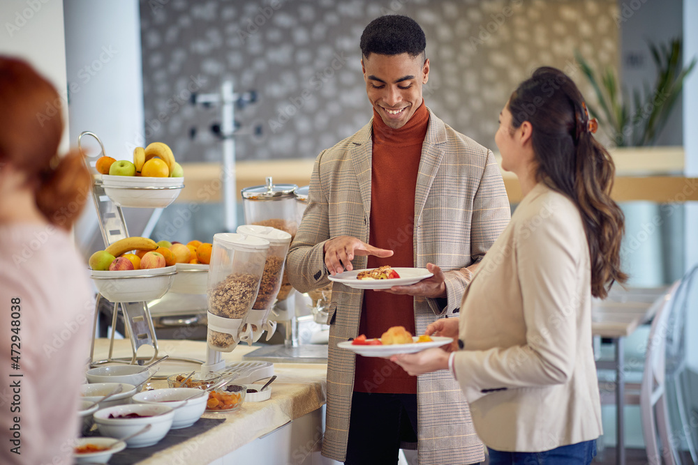 A young man is having a friendly conversation with female colleague while helping themselves with a food at the lunch break during a business conference. Business, people, meeting, company A young man is having a friendly conversation with female colleague while helping themselves with a food at the lunch break during a business conference. Business, people, meeting, company