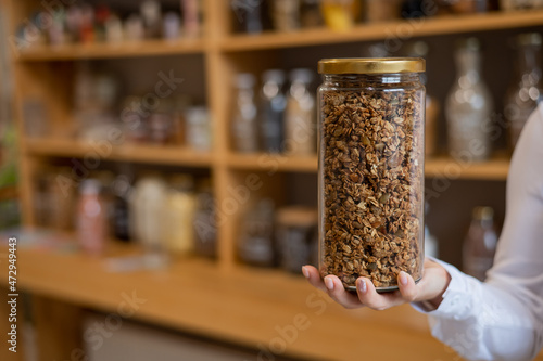 A woman holds a glass jar of granola in an eco friendly store. The concept of a grocery store without plastic disposable packaging