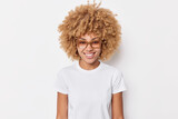 Portrait of pretty young woman with curly hair smiles happily wears spectacles casual basic t shirt has glad expression enjoysfree time poses for making photo isolated over white background.