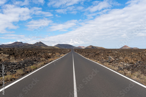 Lonely road in a straight line towards the volcanic mountain, on the Lanzarote Island. Canary Islands - Spain
