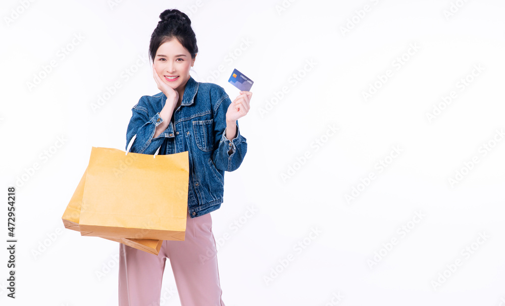 Excited cheerful smile shopper asian woman wear jacket jeans holding shopping bags paper showing credit card mockup while standing over isolated white background. Payment finance electronic concept. Excited cheerful smile shopper asian woman wear jacket jeans holding shopping bags paper showing credit card mockup while standing over isolated white background. Payment finance electronic concept.